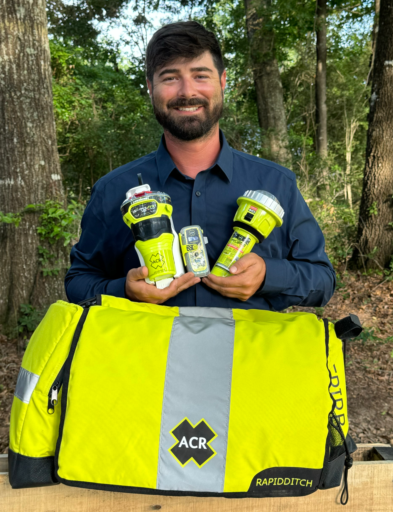A bearded man stands holding three bright green devices in front of a bag, each has the logo for ACR on it.