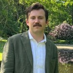 Portrait photo of NASA Ames scientist Aidan Ramey. He is standing in a green field wearing a white collared shirt.
