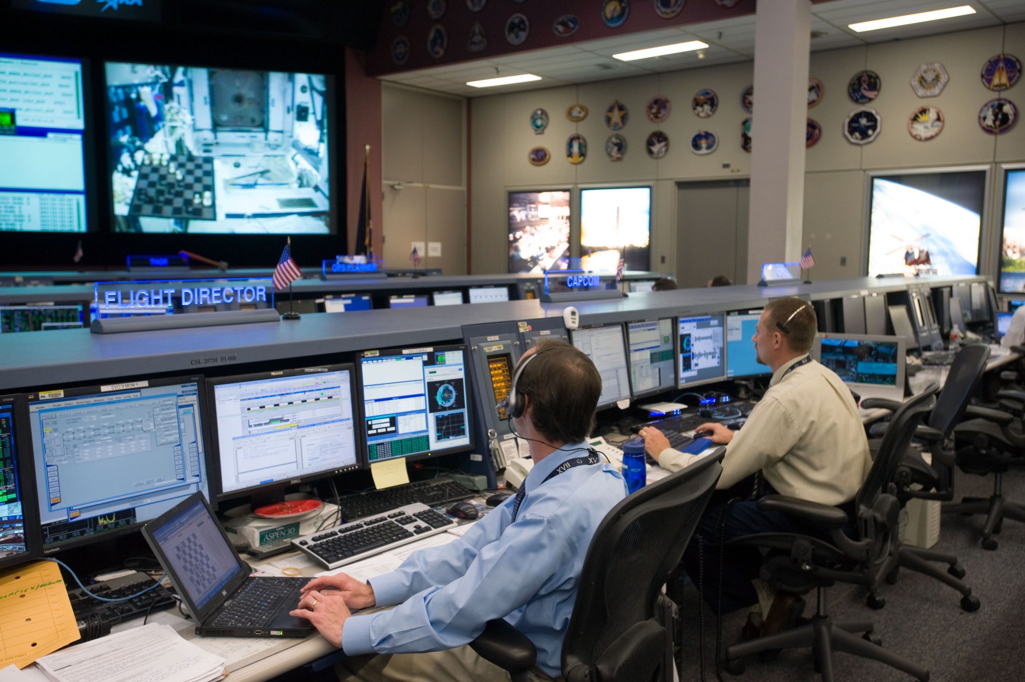 A man sitting at a desk on console with several monitors in front of him.