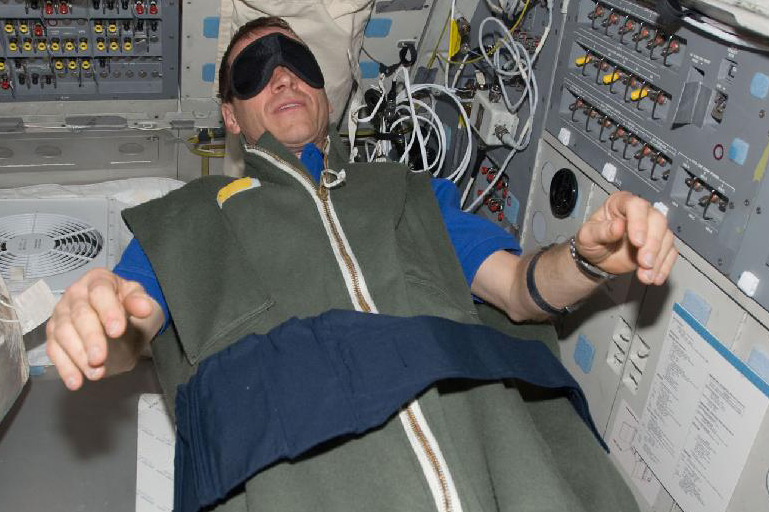Image of a NASA astronaut sleeping in the microgravity of Earth, inside the sleep quarters of the International Space Station (ISS). 