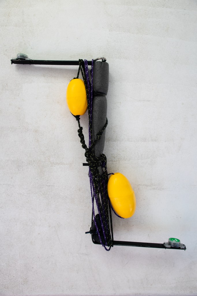 A black instrument shaped like a Z sits on a white background. A black rope wraps around the body of the instrument, with two bright yellow ellipsoids attached.