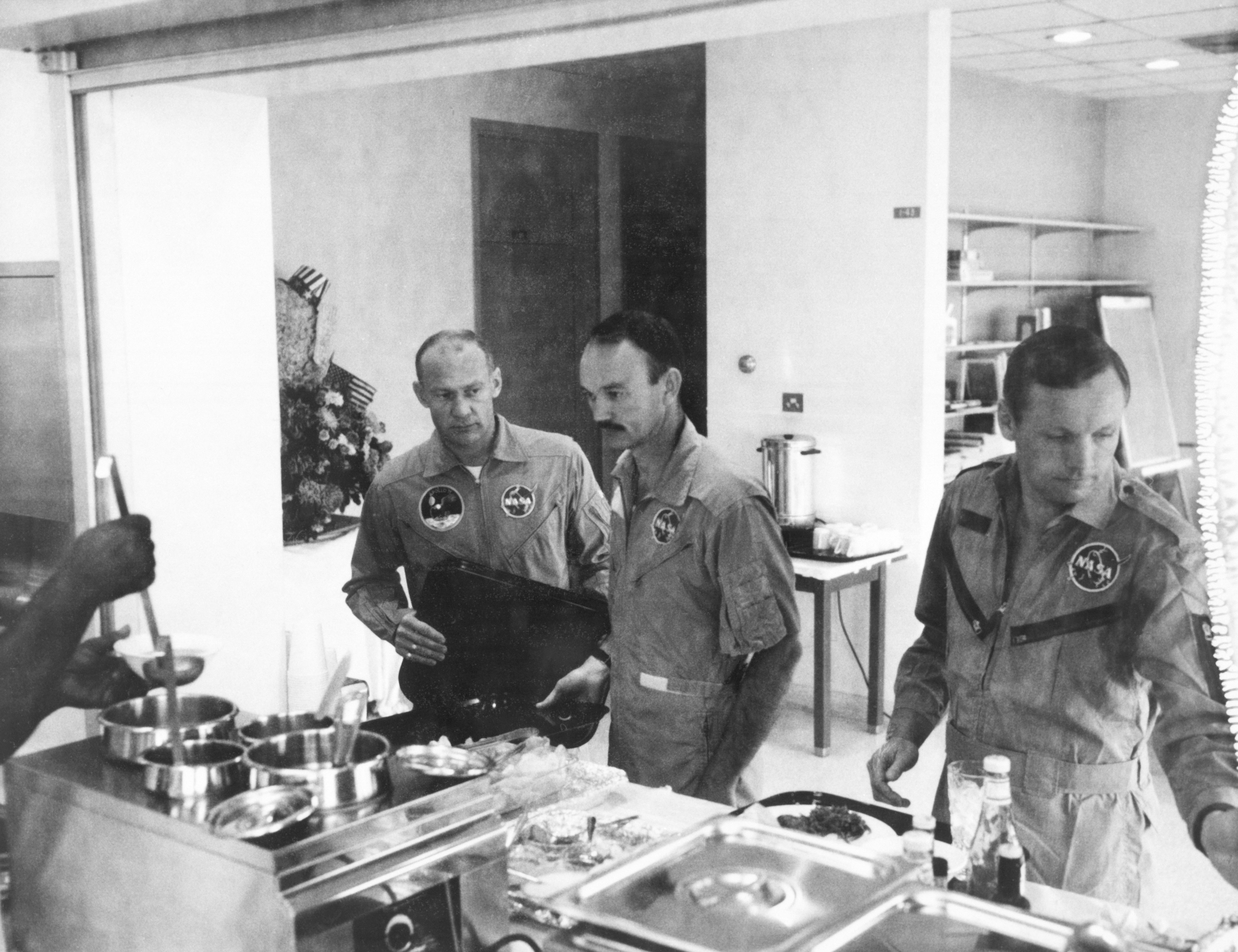 The crewmen of the historic Apollo 11 lunar landing mission stand in the serving line as they prepare to dine in the Crew Reception Area of the Lunar Receiving Laboratory