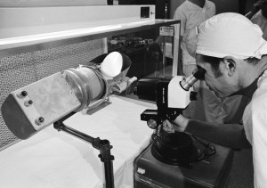 View of scientist looking at a Surveyor III components with a microscope in a Lunar Receiving Laboratory sterile vacuum cabinet.