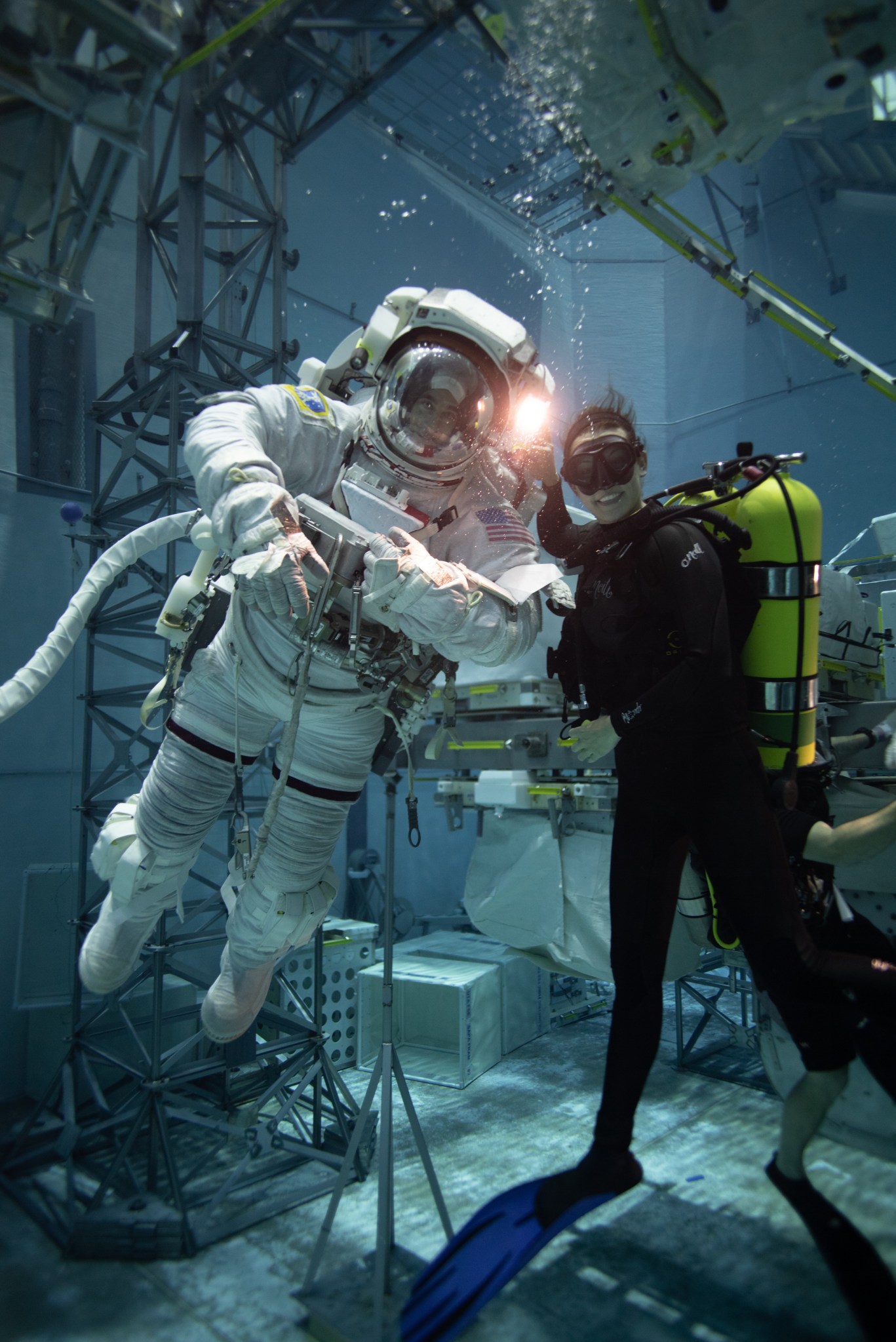 Two divers pose underwater. The diver on the left is wearing a spacesuit.