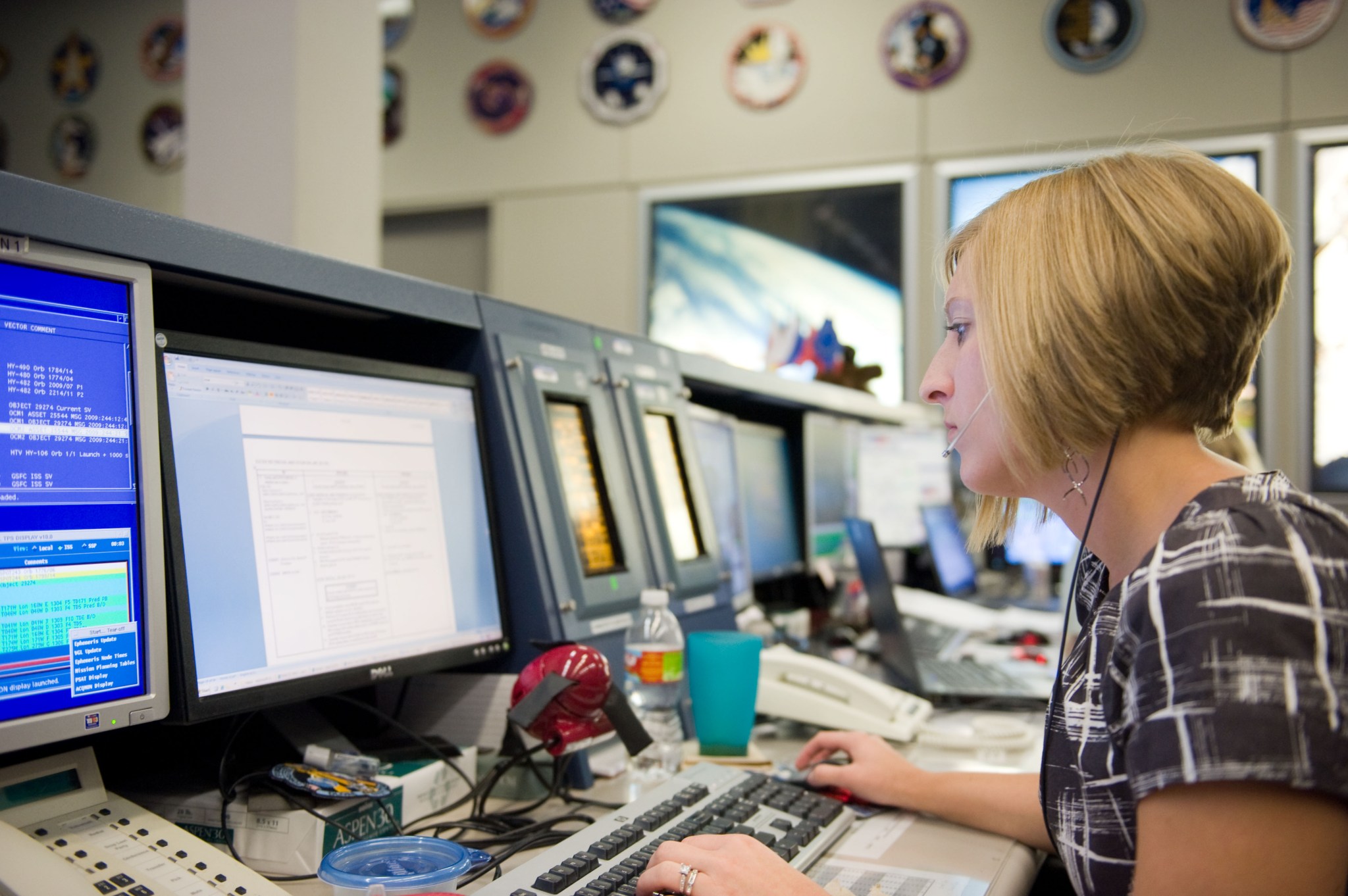 A woman sits in front of a bank of computer screens in the Mission Control Center at Johnson Space Center.