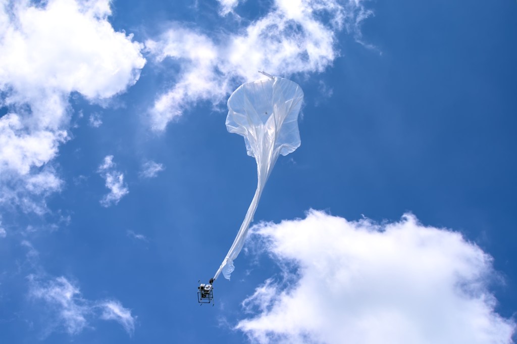 A high-altitude balloon rises into the sky with a payload attached.