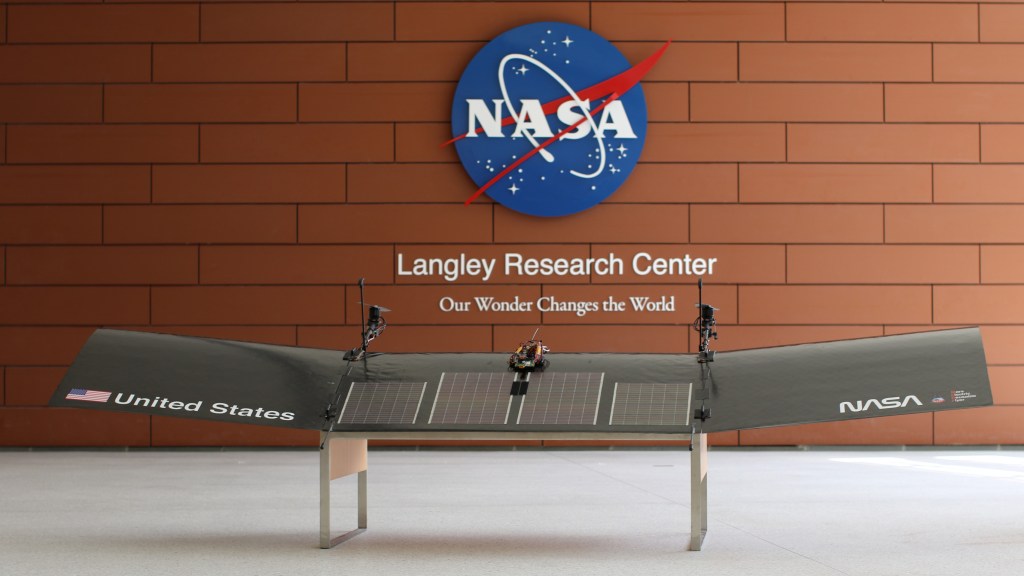 A NASA meatball is placed with "Langley Research Center: Our Wonder Changes the World" below it on a brick wall. In front of the wall is a silver scale model of MERF (Mars Electric Reusable Flyer).