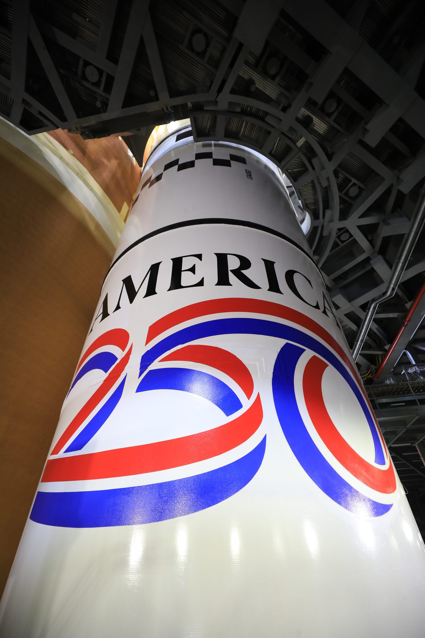 Image shows the America 250 logo in black, red, blue colors painted on the white solid rocket boosters of NASA's SLS (Space Launch System) rocket at NASA's Kennedy Space Center in Florida on Dec. 1, 2025.