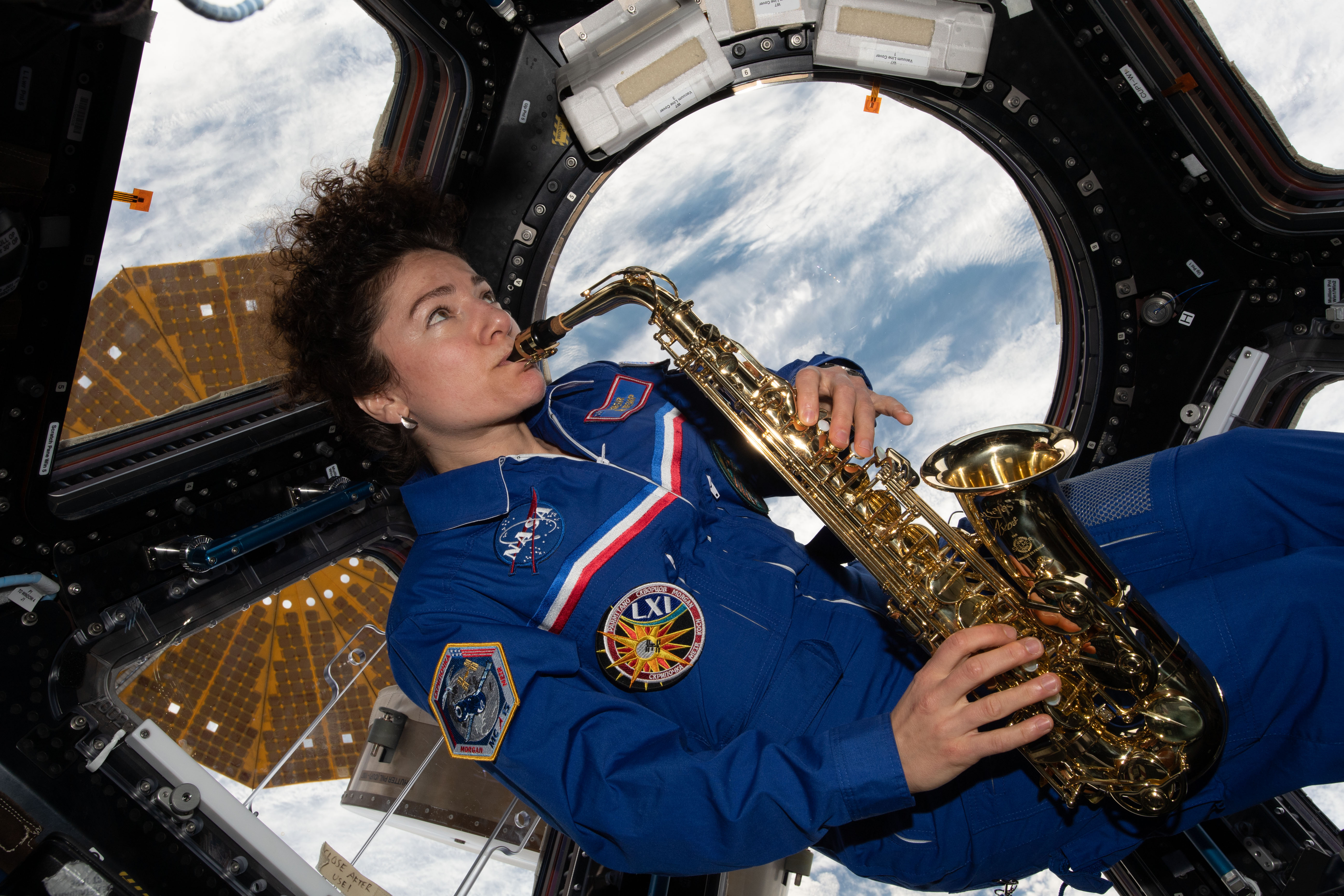 A woman in a blue flight suit plays the saxaphone aboard the space station.