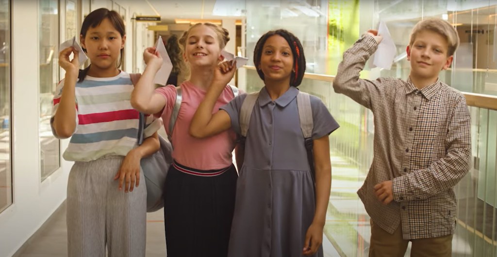 A diverse group of four children throwing paper airplanes.