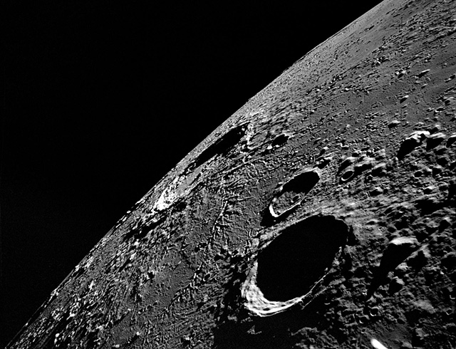 An Apollo 12 high-oblique view of the lunar nearside looking northeast toward the crater Copernicus (in center near horizon), as photographed from lunar orbit. The shaded crater in the foreground is Reinhold. Reinhold B is the crater next to Reinhold which as the small crater in the center of it. Also, visible is the keyhole-shaped crater Fauth near the crater Copernicus.