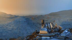 The Curiosity rover is visible at the bottom right of this panorama image. The rover is at the top of a ridge referred to as a boxwork formation. The sky ahead of it is hazy; it's red on the left and blue on the right.