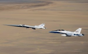 NASA’s X-59 flies above the Mojave Desert with a NASA F-15 chase aircraft nearby.