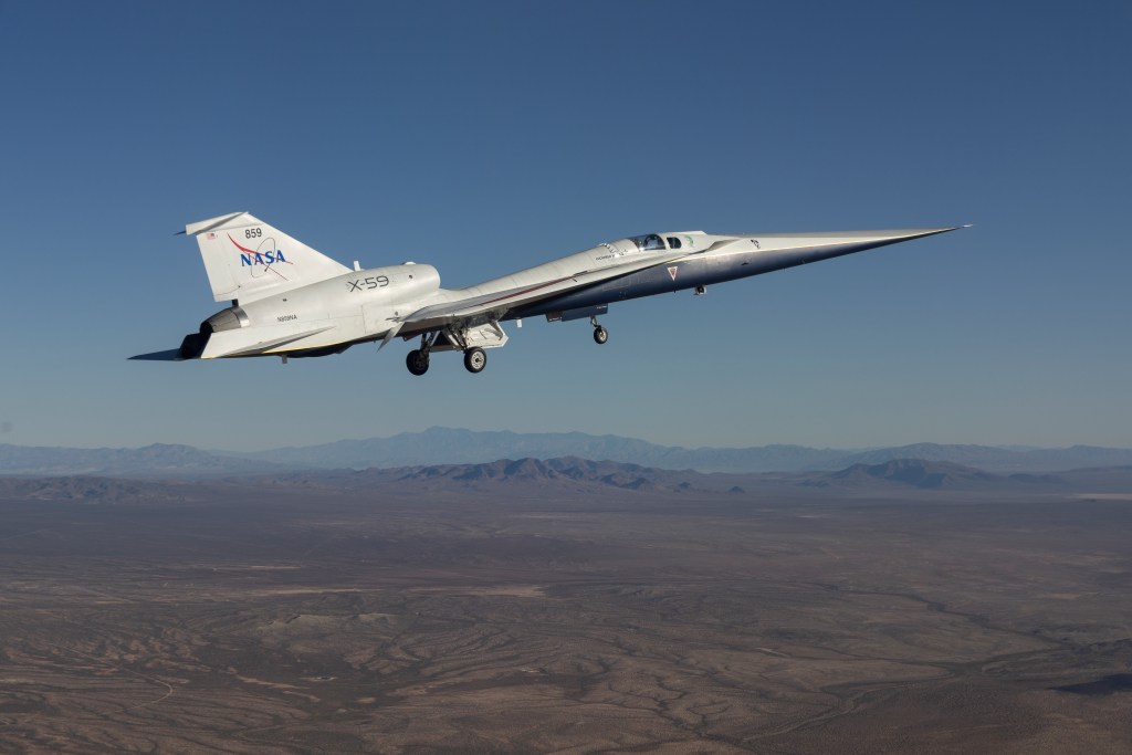 Image of a sleek, white airplane with a sharp, pointed nose flies above arid mountains. The plane's wheels are down. NASA is painted in blue lettering on its tail.