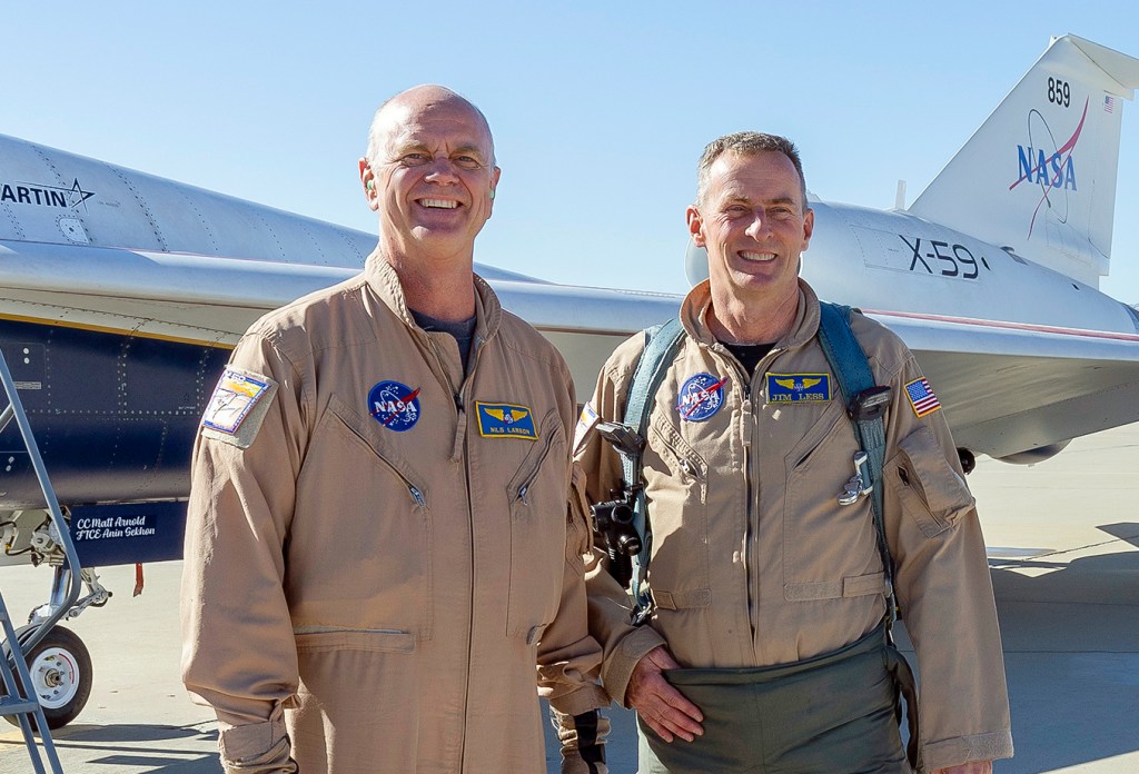 Two NASA pilots wearing flight gear pose in front of the X-59 experimental aircraft.