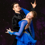 A male dancer in a black suit and a female dancer in a blue ballroom gown are captured mid-dance, with the woman leaning back gracefully.