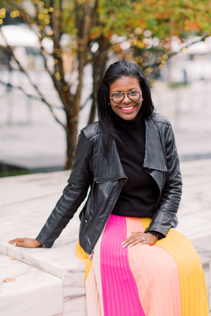 Carimanda sitting outside wearing a black jacket and glasses.