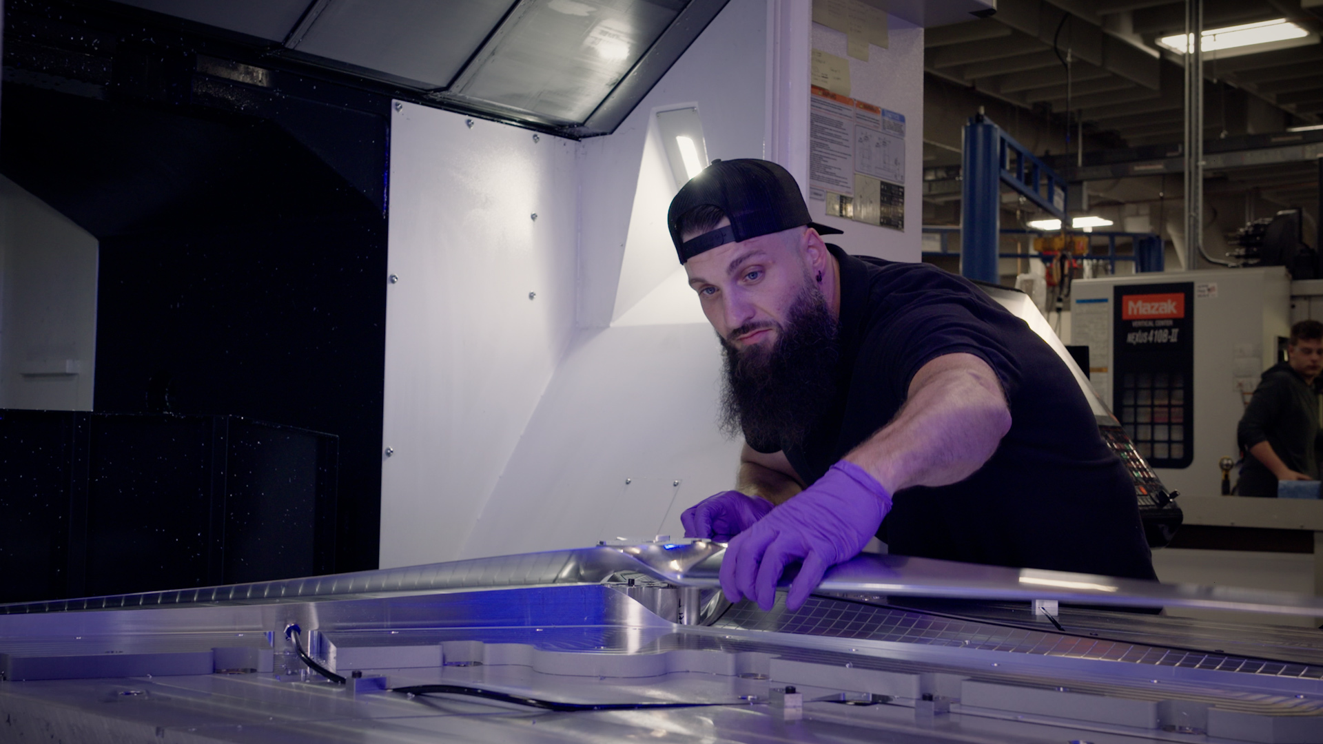 A man wearing dark clothes and purple gloves works on a silver rotor on a table.