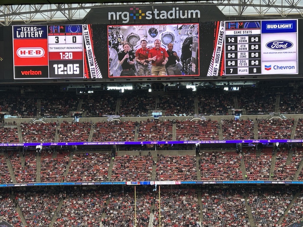 An image of a full stadium at a football game with a video playing on the jumbotron.