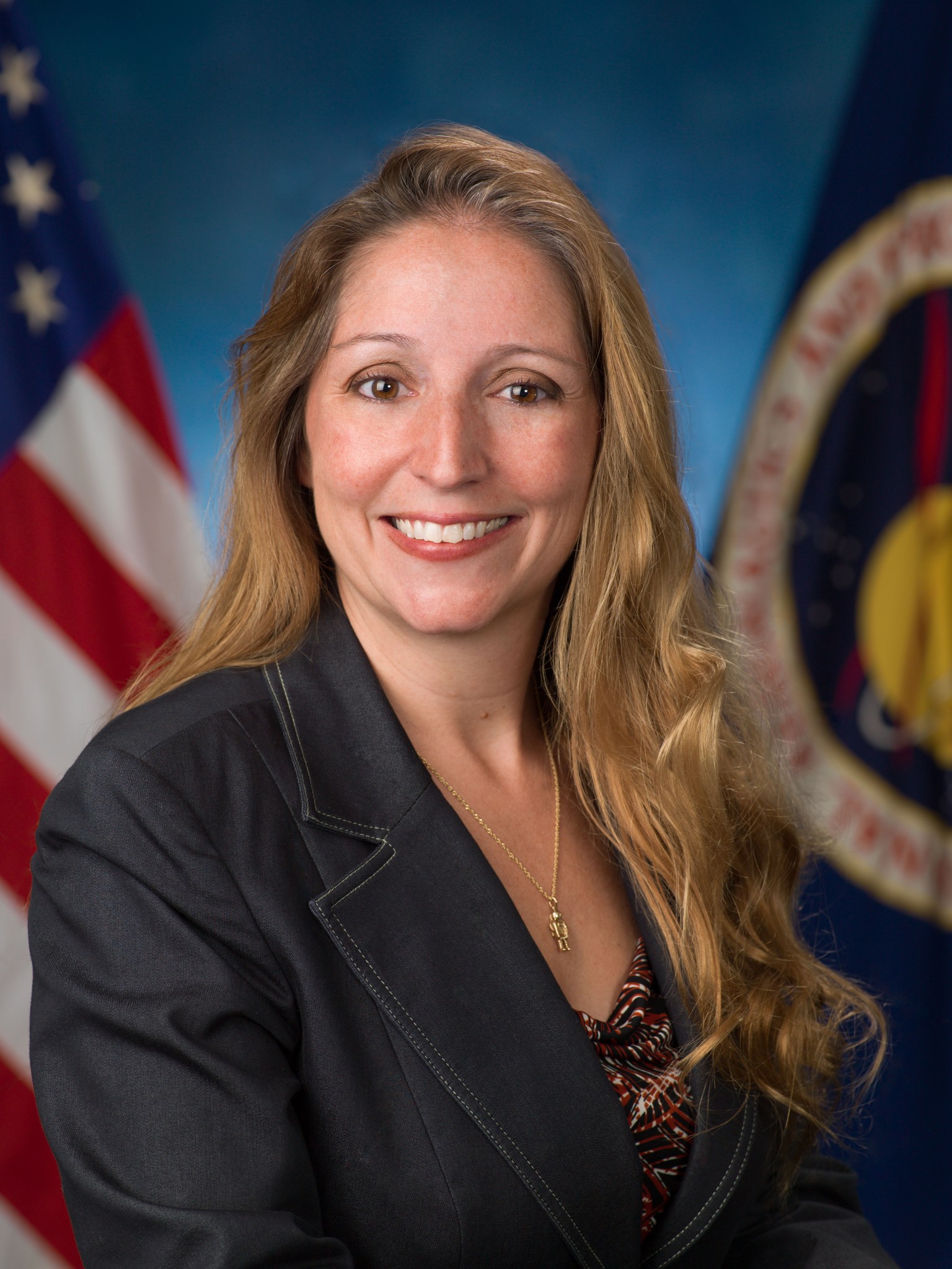 A woman poses in a black suit in front of the U.S. flag (left) and the NASA flag.