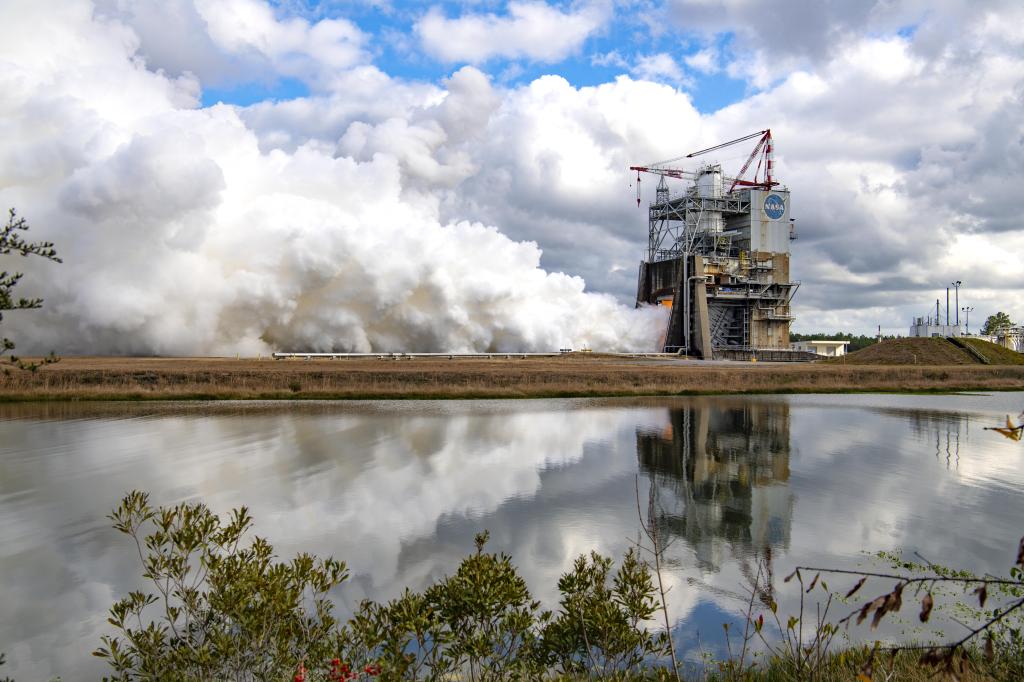 a reflection of the Fred Haise Test Stand during a hot fire test is captured on nearby body of water