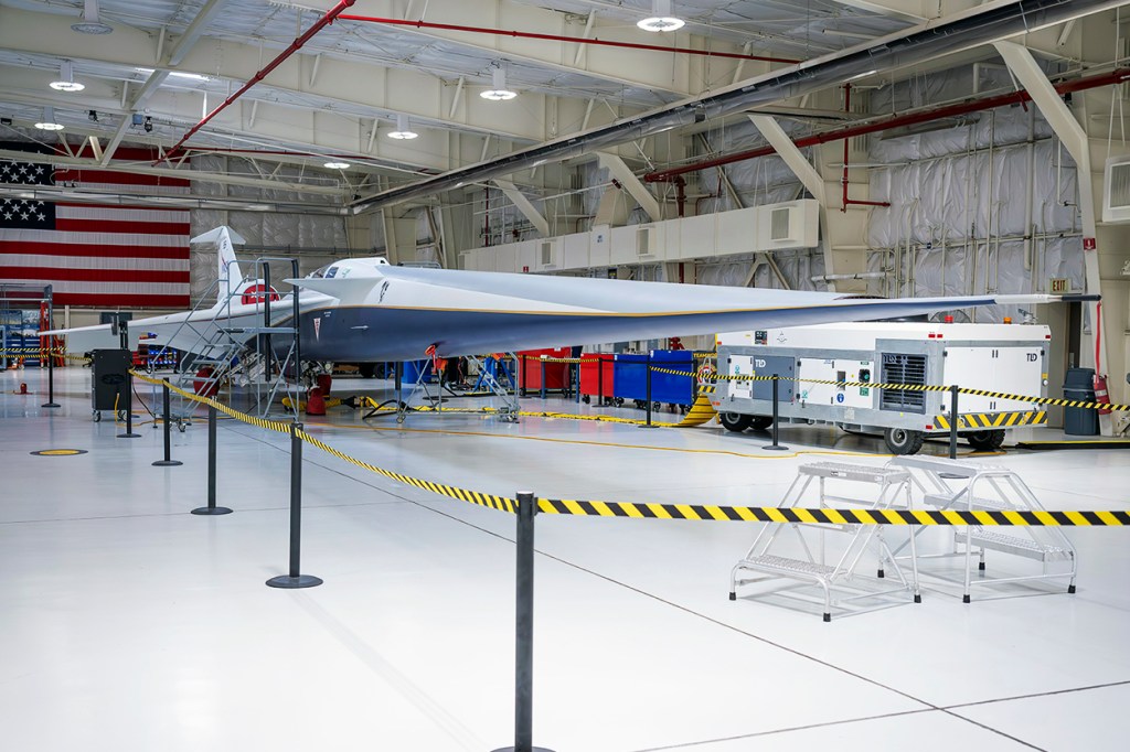 A blue and white supersonic jet with red trim sits inside a newly renovated hangar.