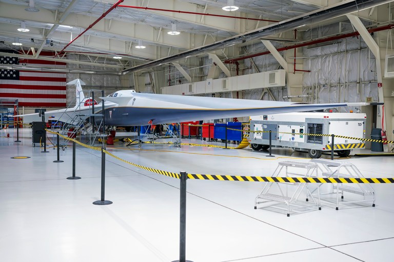 A blue and white supersonic jet with red trim sits inside a newly renovated hangar.