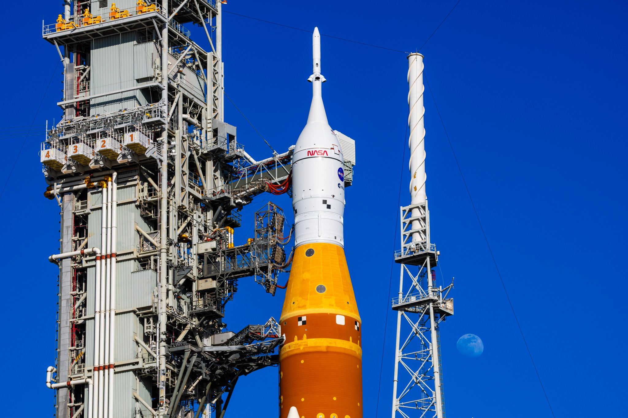 The Moon is seen behind the SLS (Space Launch System) and Orion spacecraft, atop the mobile launcher on January 28, 2026. The rocket is currently at Launch Pad 39B at NASA’s Kennedy Space Center in Florida, as teams are preparing for a wet dress rehearsal to practice timelines and procedures for the launch of Artemis II. 508 Description:The Moon is seen shining over the SLS (Space Launch System) and Orion spacecraft, atop the mobile launcher on January 29, 2026. The rocket is currently at Launch Pad 39B at NASA’s Kennedy Space Center in Florida, as teams are preparing for a wet dress rehearsal to practice timelines and procedures for the launch of Artemis II.