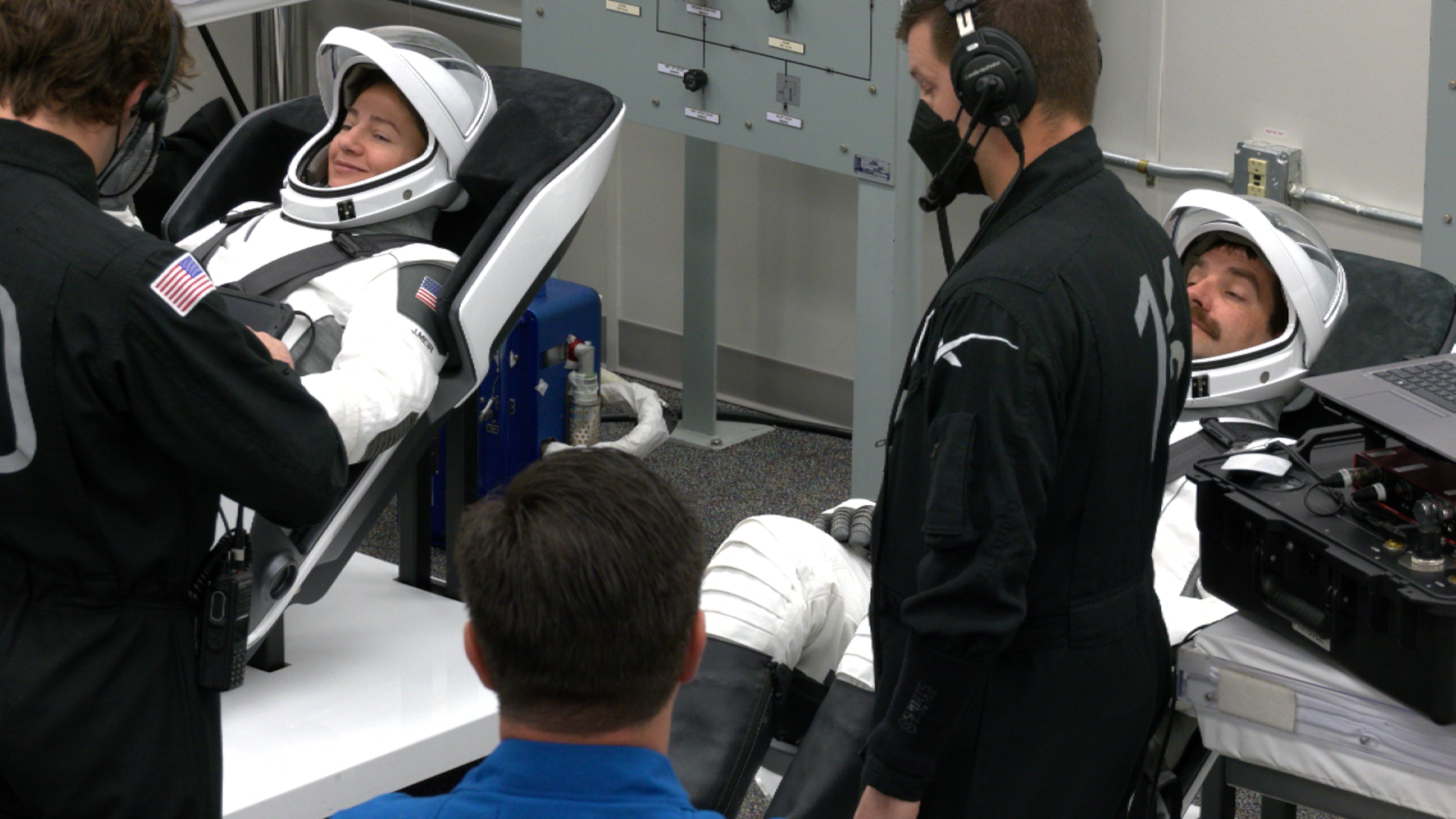Image shows two NASA astronauts in their white and black SpaceX suits undergoing suit leak checks ahead of launch to the International Space Station on Friday, Feb. 13, 2026. Photo credit: NASA