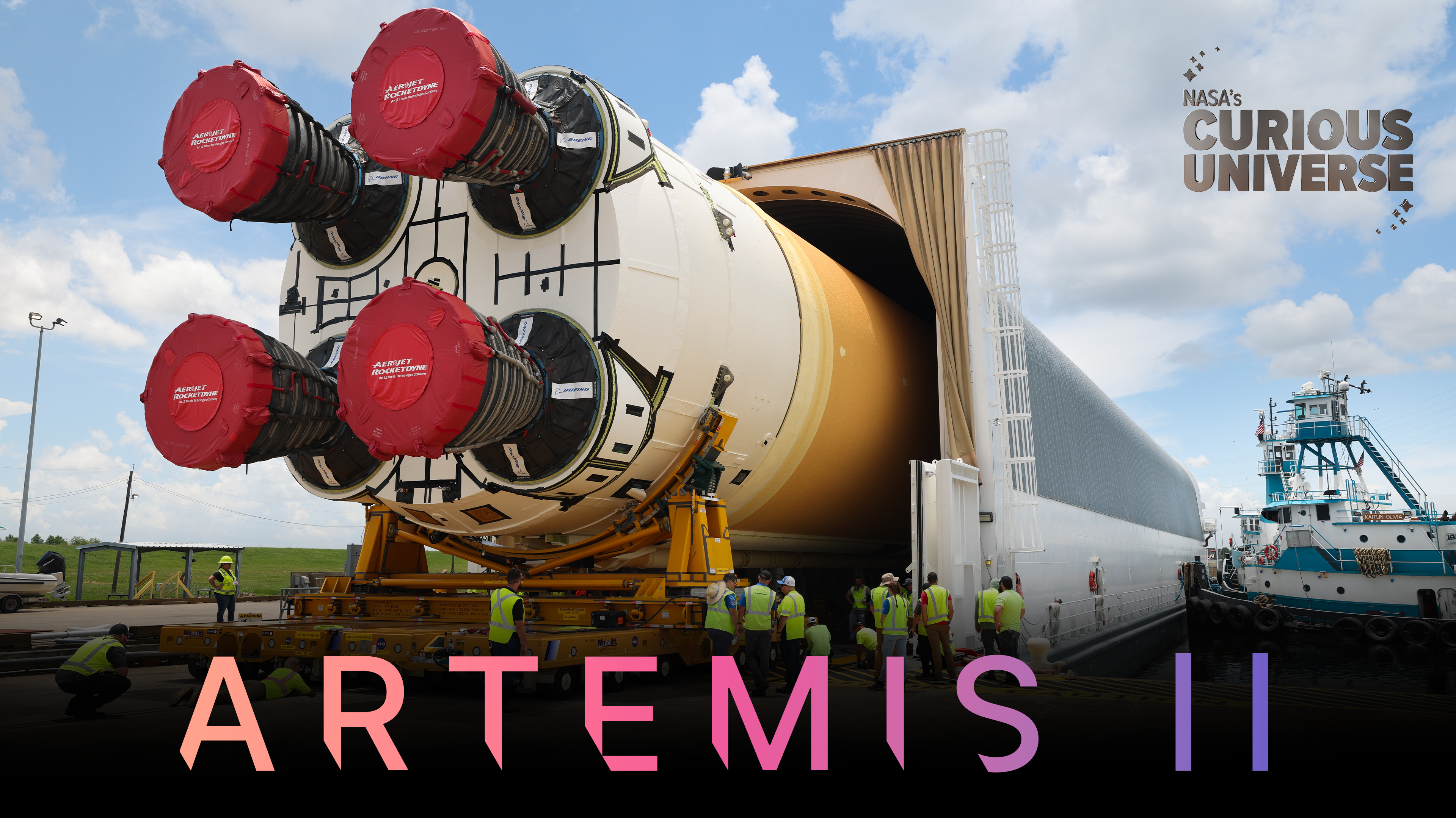 NASA's Space Launch System rocket is seen being transported by barge. A team of workers in yellow, high-visibility vests inspects the rocket. The Curious Universe logo is visible in the upper right corner and "Artemis II" is spelled across the bottom in large type.