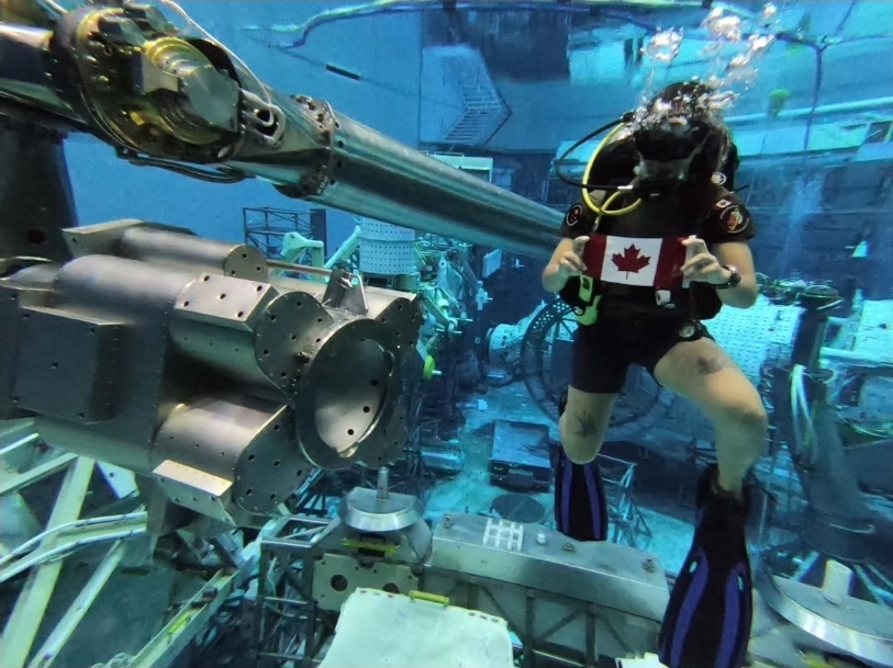 A person in a dive suit holds a Canadian flag underwater.