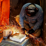 A person sanding a piece of metal with sparks flying