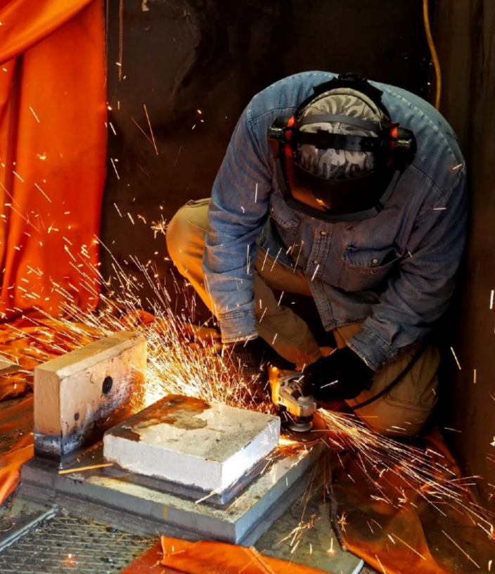 A person sanding a piece of metal with sparks flying