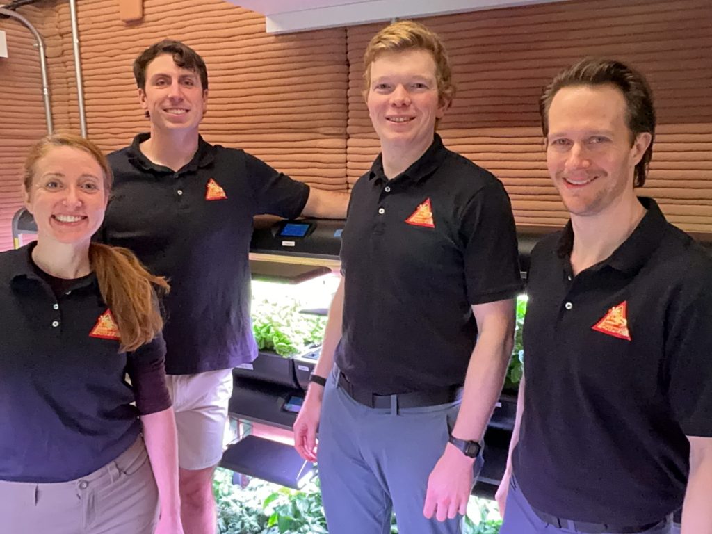 The Crew Health and PerformCHAPEA Mission 2 crew stand in front of their habitat’s garden, marking 100 days inside the habitat (from left: Ellen Ellis, Ross Elder, James Spicer, Matthew Montgomery).