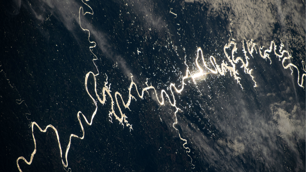 Sunlight can be seen glinting off the winding rivers across the Pampas grasslands of South America. The light forms a long winding shape from right to left across a dark blue background with patches of white clouds.