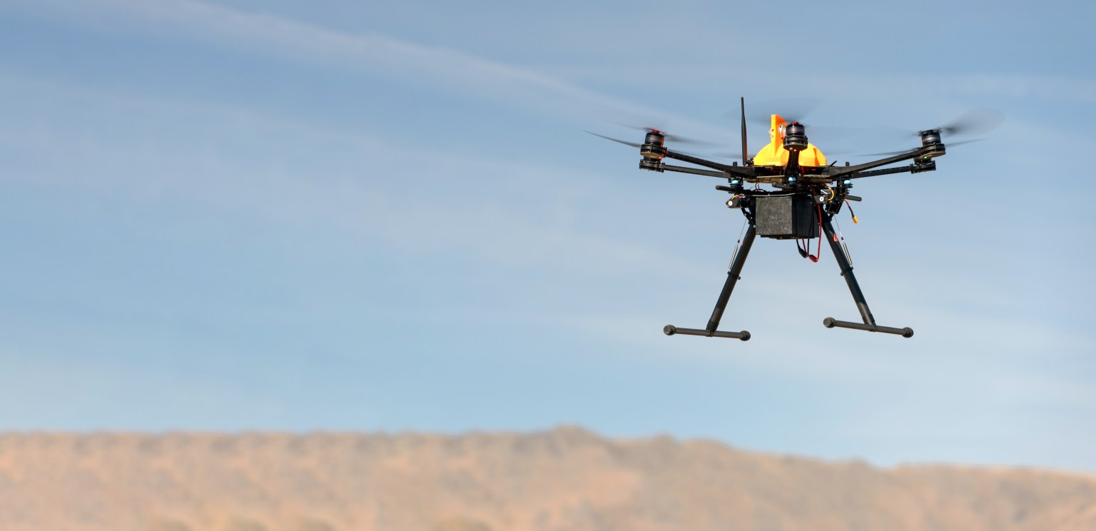 A black and yellow drone hovers over the ground.