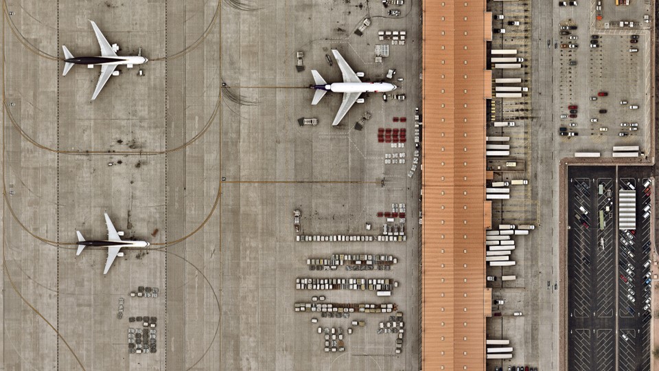Overhead picture of an airport with three airplanes visible and a number of cargo containers and shipping trucks.