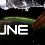 A vibrant green aurora is visible on the arched horizon of the Earth. A portion of the space station is visible on the top part of the picture and one of the space station’s solar array wings is in front of the Earth.