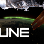 A vibrant green aurora is visible on the arched horizon of the Earth. A portion of the space station is visible on the top part of the picture and one of the space station’s solar array wings is in front of the Earth.