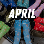 A group of people wearing different colorful socks posed in a circle with their feet all facing the center. They are floating in the picture because they are on the International Space Station on orbit.