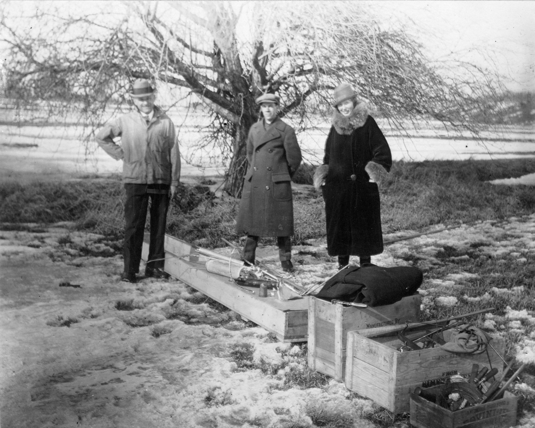 black-and-white photograph of a trio of people standing outdoors with wooden crates at their feet