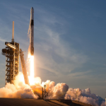 A picture of a rocket and capsule launching off the pad with plumes coming out the bottom during the daytime.