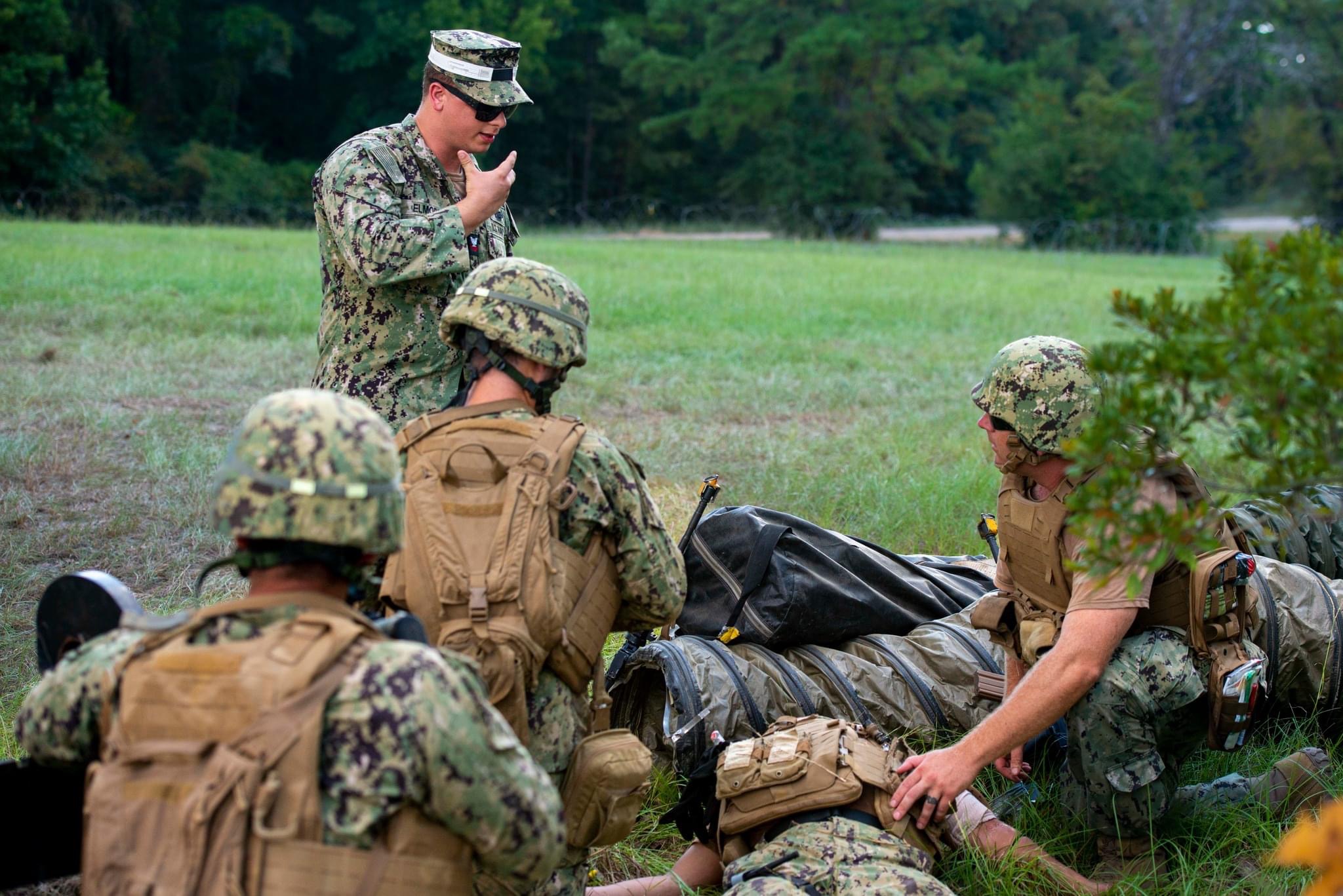 U.S. Navy personnel conduct a field training exercise while assisting a simulated casualty in an outdoor environment.