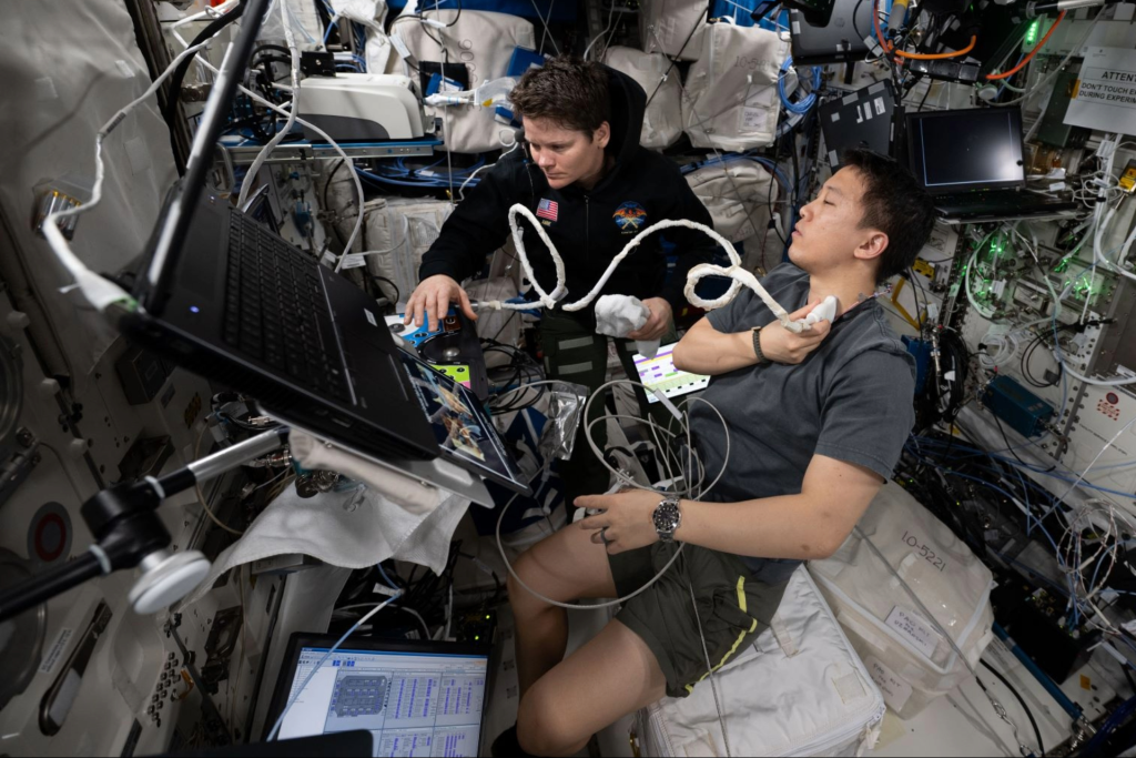 NASA astronaut Anne McClain assists NASA astronaut Jonny Kim with an ultrasound scan aboard the International Space Station. Ultrasound scans help scientists monitor blood flow changes in space.