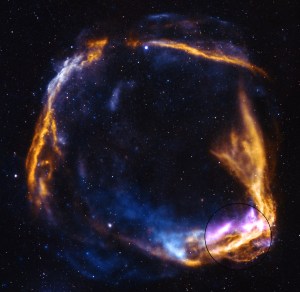 A fiery orange supernova remnant has the shame of a ring breaking apart. The outer rim is highlighted in purple at bottom right. There are stars dotting the darkness of space.