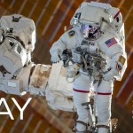 An astronaut in a white spacesuit is shown being maneuvered by the Canadarm2, which is attached to the space station, during a spacewalk.