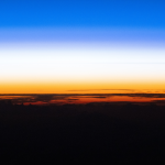 An orbital sunset silhouettes the cloud tops above the Pacific Ocean as the atmosphere along the horizon fades from orange to white, then to blue, in this photograph taken from the International Space Station while it orbited 262 miles above Earth.
