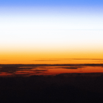 An orbital sunset silhouettes the cloud tops above the Pacific Ocean as the atmosphere along the horizon fades from orange to white, then to blue, in this photograph taken from the International Space Station while it orbited 262 miles above Earth.
