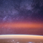 The Milky Way spans the night sky above a bright orange-yellow airglow that blankets the city lights along the east coast of Africa, from Kenya to Somalia.