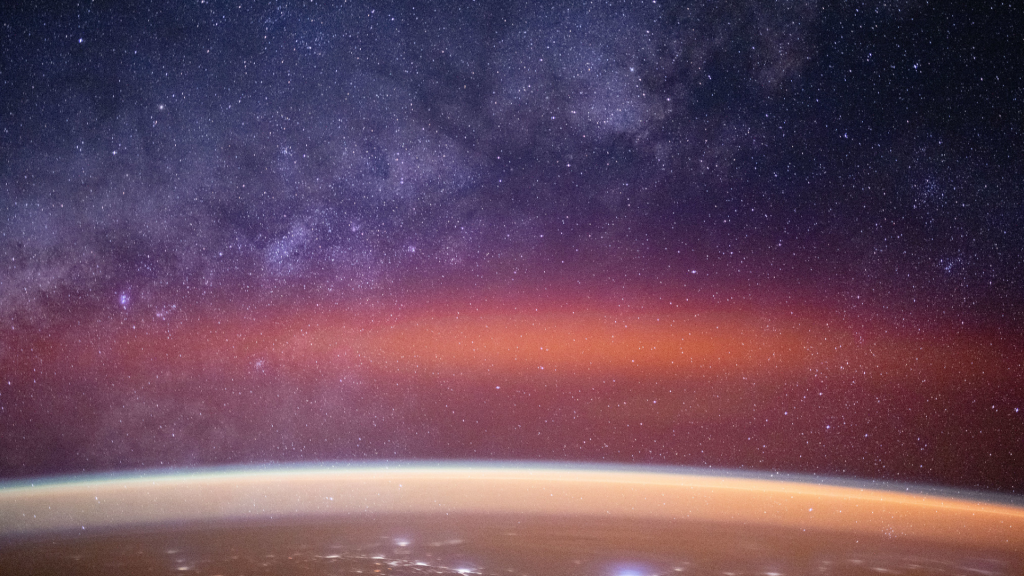 The Milky Way spans the night sky above a bright orange-yellow airglow that blankets the city lights along the east coast of Africa, from Kenya to Somalia.